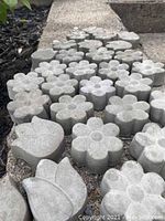 Concrete garden accent stones arranged in rows on a concrete ledge, showing flower and leaf shapes and weathered surfaces
