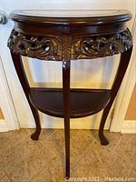 Front view of the half moon accent table showing the carved floral apron and curved legs.