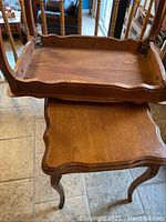 View showing one table upside down on top of the other to display underside and solid wood construction with scalloped edge detail.