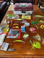 Fishing tackle box with assorted lures, spinnerbaits, soft plastic baits, fishing weights, and fishing line displayed on a wooden table