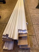 Stack of white pre-primed MDF casing pieces with detailed molding edges, showing thickness and layered profile on tile floor.