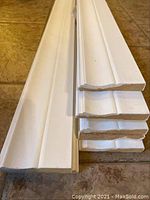 Eight pieces of white MDF baseboard trim stacked on tile floor, showing decorative profile and clean cut ends.
