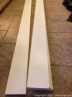 Two white MDF moulding boards laid side by side on a tiled floor showing their length and width.