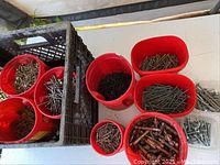 Red buckets filled with assorted nails, screws, and bolts arranged on a white surface with a milk crate holding some buckets.