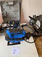 Photo showing the Mastercraft jigsaw, Ryobi drill in case, and Mastercraft compound saw together on a table with cords tangled and tools dusty.