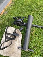 View of the black Toro leaf blower/vacuum unit with collection bag and blower tube laid on grass.