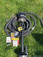 Mastercraft sump pump with coiled black discharge hose and pipe fittings laid out on grass.
