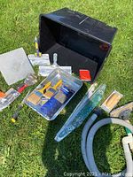 Full view of drywall and painting tools laid out on grass including hawk, saw, paint tray with brushes, putty knives, and sanding tool