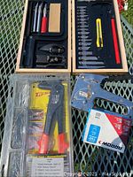Complete view of wooden box with blades and hand knife on left and right compartments, rivet tool with rivet kit in packaging, metal hand stapler with red grips and staple boxes on right.