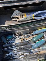 Photo of black toolbox showing an adjustable wrench and various screwdrivers inside, displaying degree of rust and dirt.