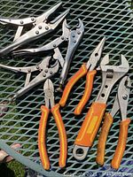 Overview of the lot showing multiple locking pliers, needle-nose pliers, and adjustable wrench with orange grips.