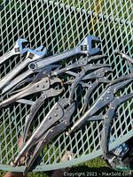 Photo showing multiple locking wrenches and three crescent adjustable wrenches on green metal mesh surface.