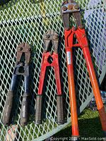 Three bolt cutters displayed on metal mesh table, sizes 12, 14, 24 inches, various handles and surface rust visible