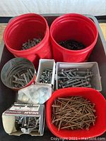 Overview of multiple red buckets and containers filled with assorted galvanized carriage bolts, washers, nuts, deck screws, and concrete screws.