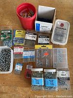 Overview of fasteners including multiple packages and loose screws in containers, shows brands HandyPak and Gold, plastic wall plugs, hollow wall anchors, and screws.
