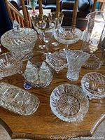 Crystal candy dish with lid, stemmed glasses with gold rims, small bowls, and fluted vase arranged on a wooden table.