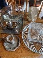 Full lot view showing various glass platters, silver plate tray, cream and sugar cups, candlestick holders, and scalloped ball dish on wooden surface