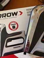 Close up of Arrow stapler and nailer tool next to original box showing partial branding and tool handle.