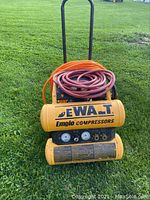 Front view of the yellow DeWalt Emglo air compressor with two air hoses coiled on top, showing gauges and output ports.