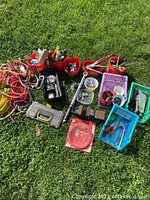 Overall assortment of hand tools, ropes, buckets of tools, hardware, and tool case spread on grass.
