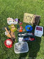 Wide shot showing all items included in the lot spread on grass: vintage heater, blue coiled cable, wooden rulers, plastic containers with screws and hardware, various tools and accessories.