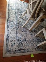 Top-down view of rug under dining chairs showing faded medallion border and floral pattern in light blue, gray, cream