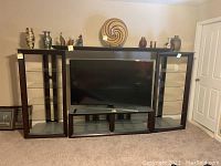 Front view of the entire media center showing the two tall display pieces, center TV stand, and top wood piece with decorative items on top.