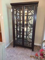 Front view of dark wood display cabinet with decorative glass doors and circular wood design, standing on carpeted floor.