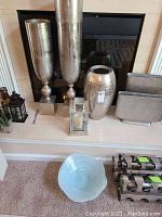 Wide view of large and medium tall metallic vases, small vase, ceramic bowl and two Ikea wine holders visible on floor beside them.