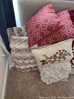 Throw pillows stacked on carpet with visible designs and accompanying throws.