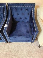 Front view of the dark blue velvet armchair showing tufted back and nailhead trim