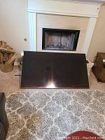 65-inch Samsung LED TV screen facing forward, leaning on carpet in front of fireplace.