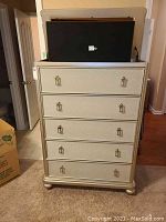 Front view of five-drawer silver metallic dresser with decorative metal pulls and bun feet