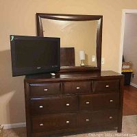 Front view of dark brown wooden dresser with seven drawers and large mirror on top.