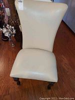 Front view of one chair showing cream upholstery and dark wood legs