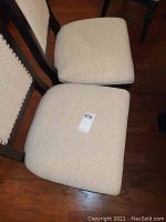 Two chair seat cushions viewed from above, showing beige woven fabric and lot sticker on one seat