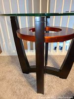 Side image showing black legs supporting a circular wooden base with a round cut-out center under a glass top.