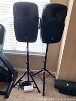 Two Proreck powered speaker cabinets mounted on Proreck adjustable tripod stands with bundled cables and power adapter at base.
