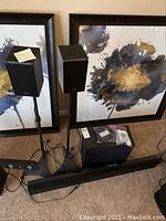 Two rear speakers on stands with subwoofer and sound bar in front, cables and remote visible