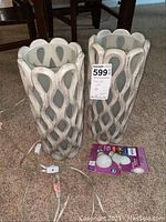 Pair of white lattice design table lamps shown together with light bulbs on carpeted floor.