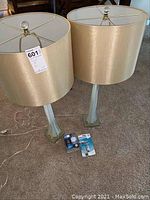 Full view of two floor lamps with beige fabric shades and lightbulbs on carpeted floor