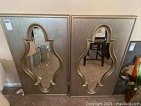 Front view of two decorative mirrors side by side against a wall showing unique shaped inset mirrors and gold frames.