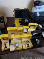 Overview of nine Invicta watches in individual yellow boxes and one empty yellow Invicta protective case on table