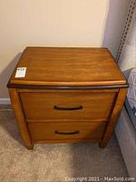 First nightstand, front view showing two drawers with metal handles, medium brown wood, some surface scratches.