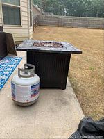 Square metal fire pit next to propane tank on concrete patio