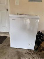 Full view of white Hisense chest freezer in a garage setting, showing front and top lid closed.