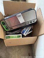 FoodSaver vacuum sealer machine with green sealing strip inside a cardboard box with multiple storage bags and containers boxed in packaging.