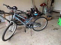 Side angle showing the full bike with grey and blue frame, 26-inch tires, knobby tread, and rear derailleur.