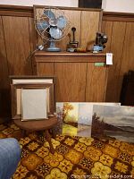 Full lot showing vintage fan on shelf with old steam iron and other items on top, footstool with empty frames, and four oilettes leaning against the wall