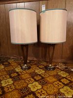 Front view of pair of 30 inch high table lamps with beige shades and wooden bases on patterned carpet.